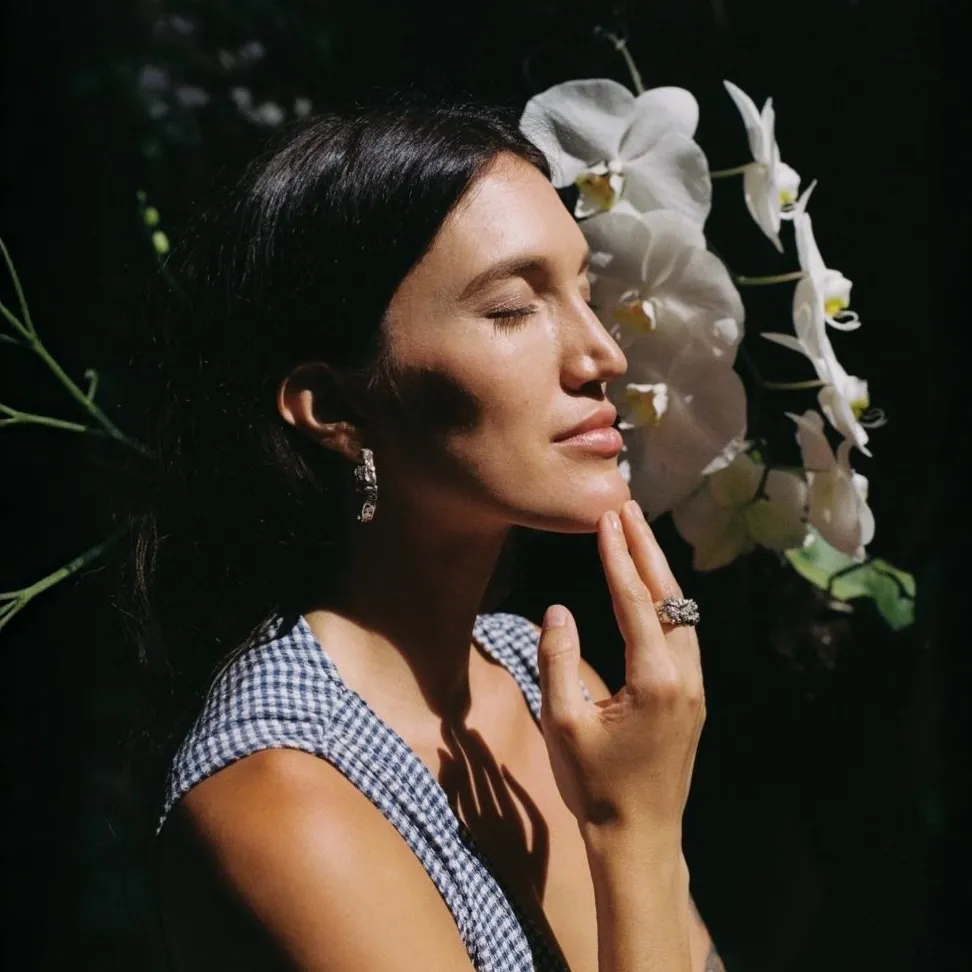 Model in a garden with orchids wearing The Navle earrings and rings
